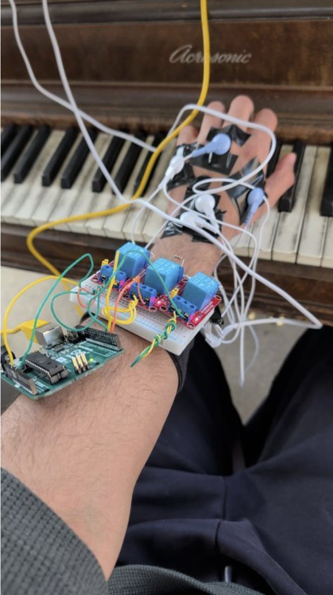 The Monday prototype worn on a forearm: EMS electrodes taped to the hand, relay board and Arduino on the wrist, in front of a piano